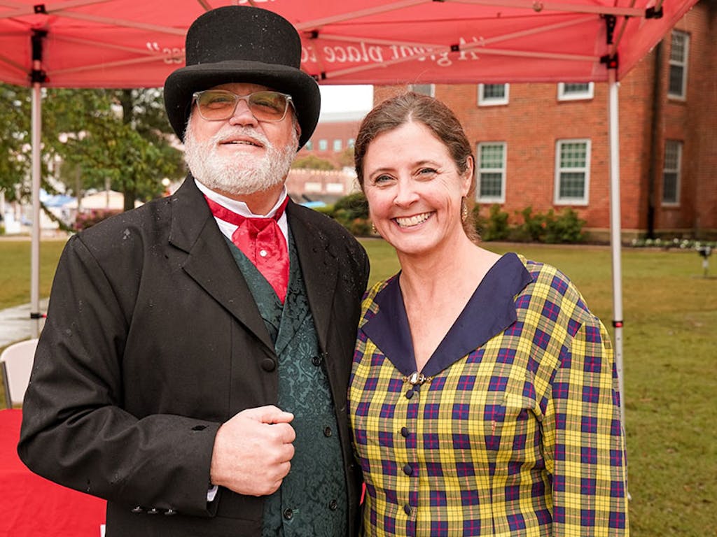 pose at the tent Man in top hat poses with women in yellow and blue checkered dress