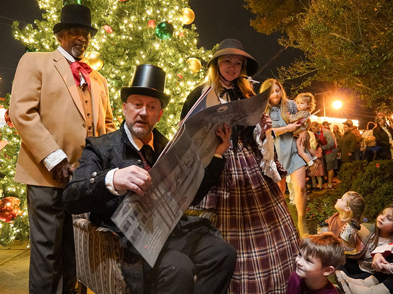 A groups of adults in full costume read to a group of children sitting on the ground