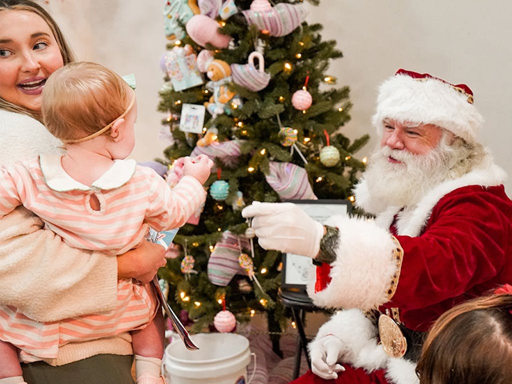 santa and child Santa seating in front of tree reaches out to a child being held by mother