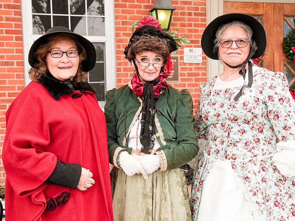three women dressed up for occasion Three women in full dress stand outside brick building