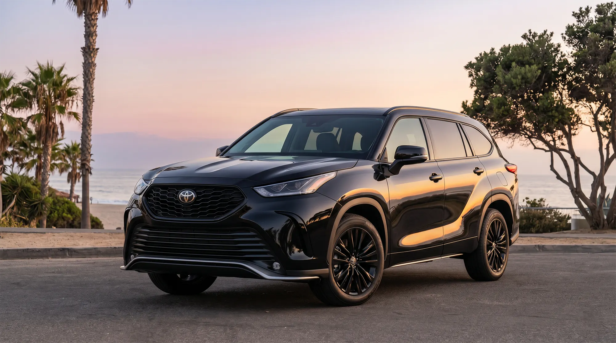 2026 Toyota Highlander in black parked on a coastal road at sunset with palm trees and ocean view in the background