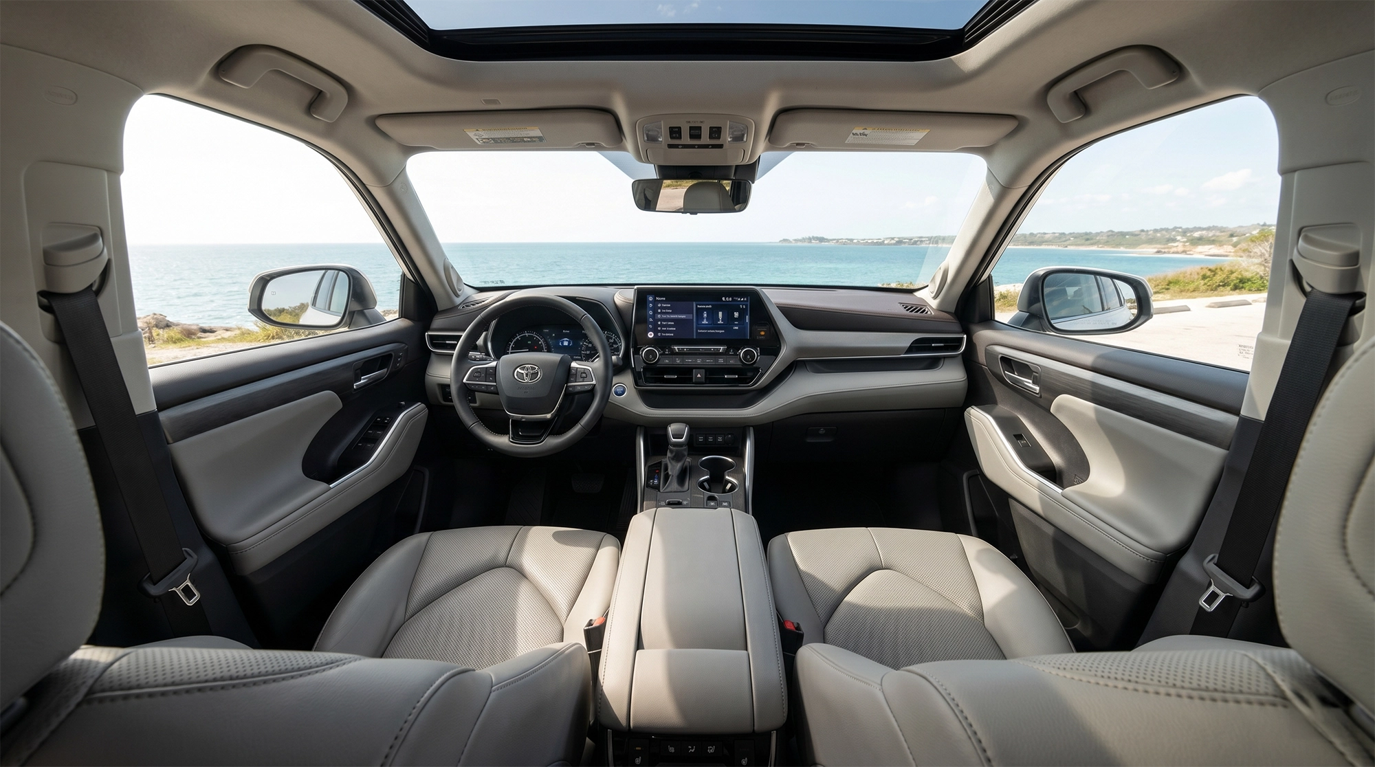 Interior of the 2026 Toyota Highlander showing dashboard, infotainment system, and front seats with ocean view through the windshield