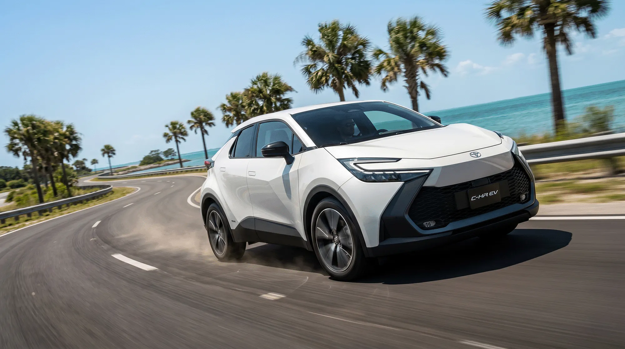 2026 Toyota C-HR electric SUV driving on a coastal road with palm trees and ocean views along the Gulf Coast