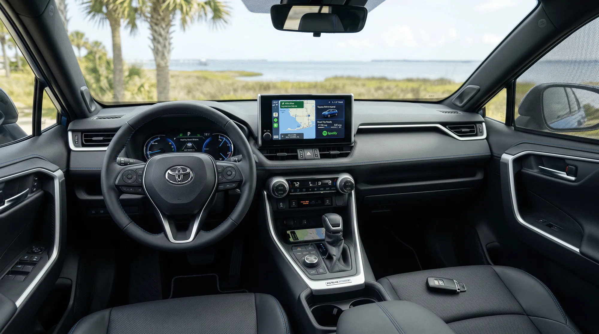 Interior of a 2026 Toyota RAV4 Hybrid showing the dashboard, steering wheel, center touchscreen, and Gulf Coast water views through the windshield.