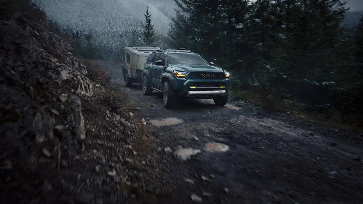25-09-22_SPTOY_4Runner_i-FORCE_MAX 2025 Toyota 4Runner i-Force Max towing a trailer on a rugged mountain trail, surrounded by rocky terrain and dense forest in misty conditions.