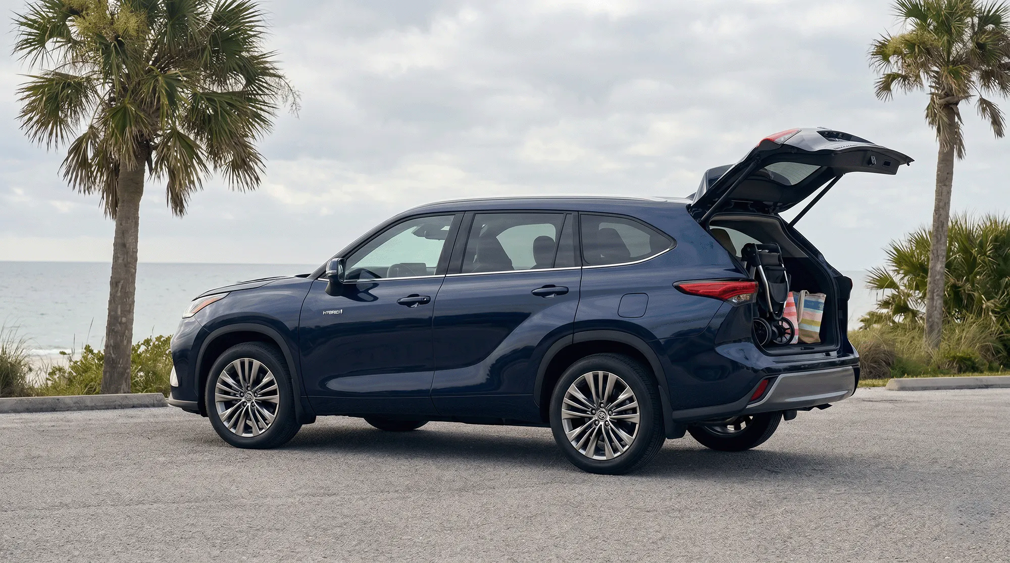 Blue 2026 Toyota Grand Highlander parked by the waterfront with the rear liftgate open and cargo loaded in back.