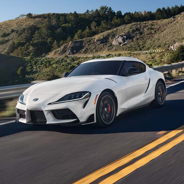 White 2025 Toyota GR Supra driving on mountain highway.