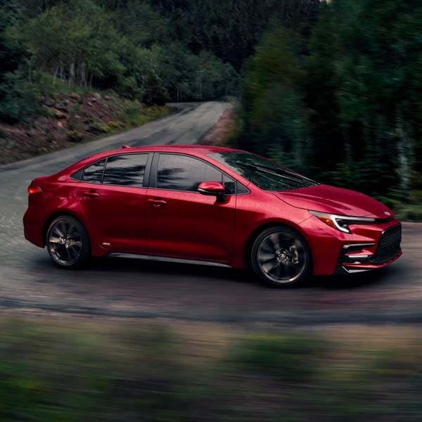 Red 2025 Toyota Corolla driving in foresty back roads.