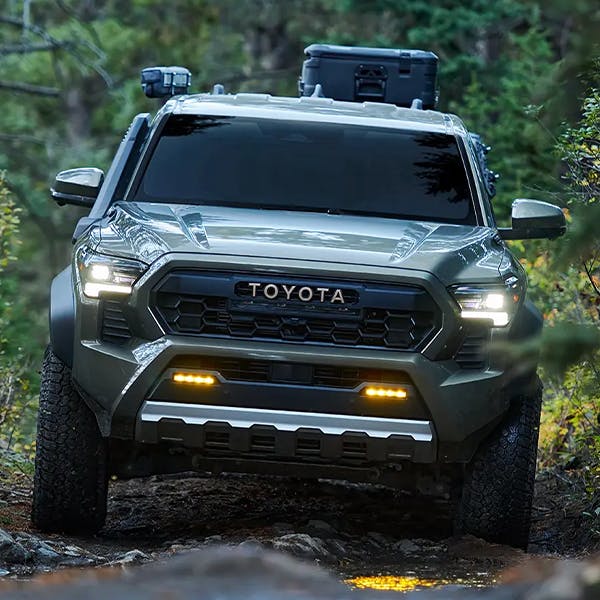 2024 Toyota Tacoma loaded with gear in the back driving down a muddy gravel road through the middle of a forrest