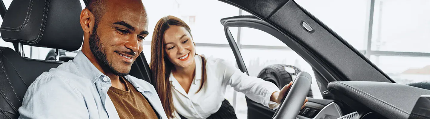 Female Sales associate explains features when man sits in driver seat.