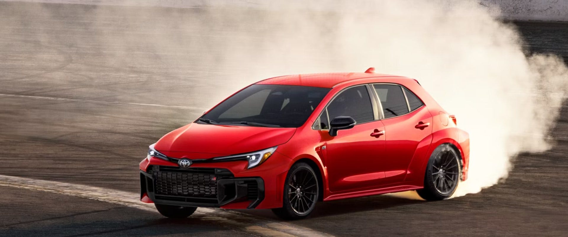 Red Toyota hatchback brakes with tire smoke