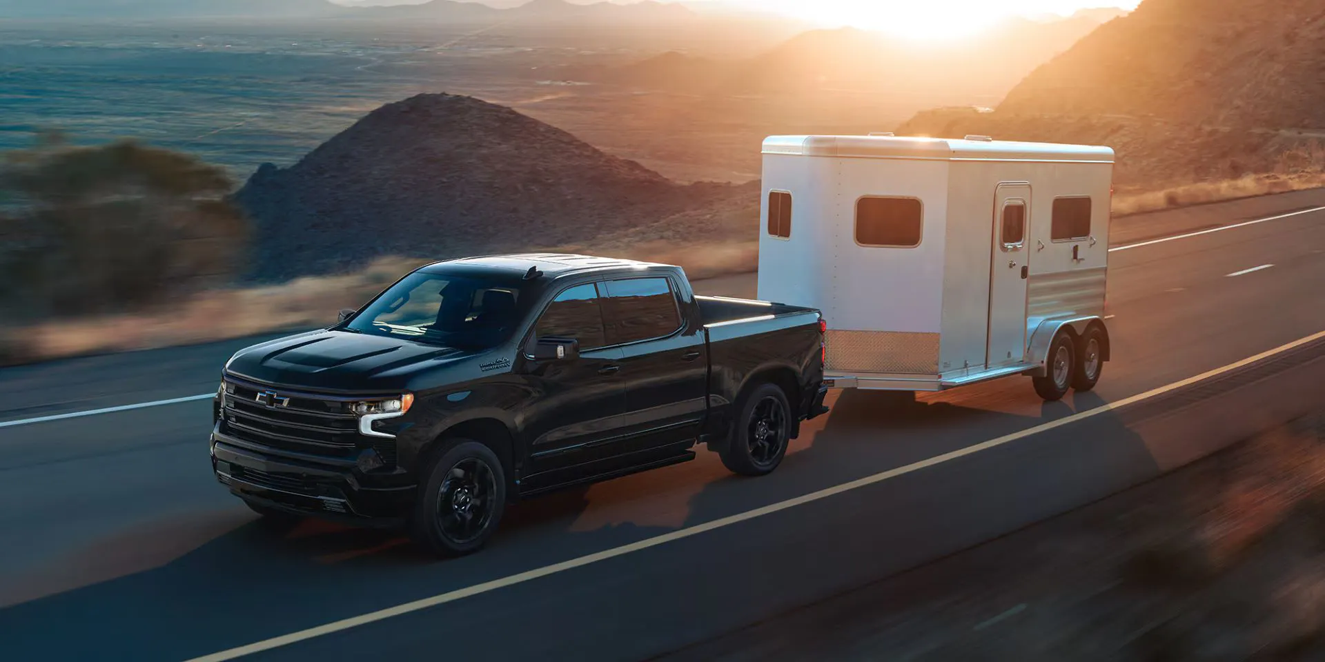A black truck pulling a trailer on the road.